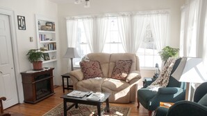 A living room with a beige sofa, a green armchair, a wooden coffee table, and a bookshelf. - Candlebay Inn (Freeport)