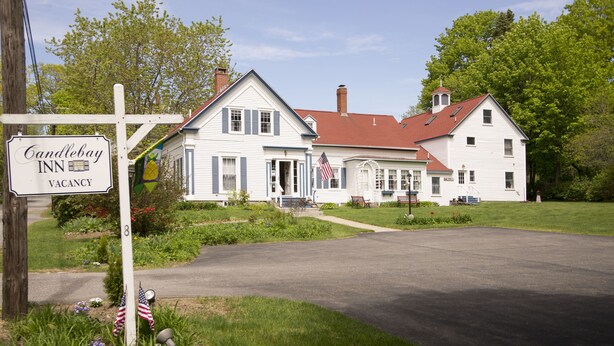 A white building with a red roof, a sign indicating a vacancy at Candlebay Inn, and an American flag. - Candlebay Inn (Freeport)