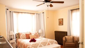 A bedroom with a bed, bedside tables, a chair, a ceiling fan, and a radiator. - Candlebay Inn (Freeport)