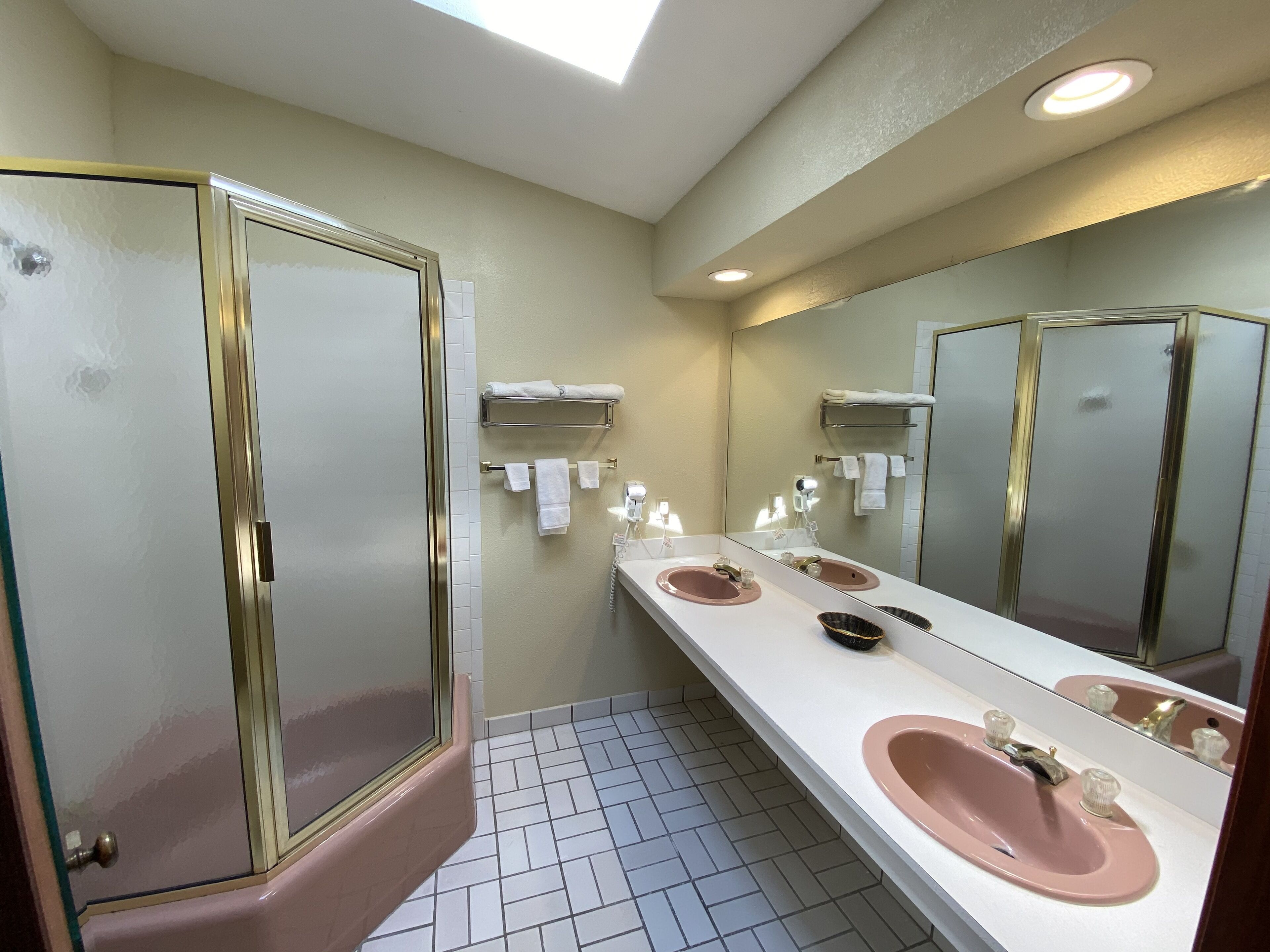 A bathroom with a large mirror, three sinks, and a shower.