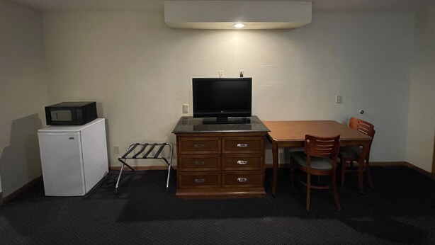 A compact room with a kitchenette, a flat-screen TV, a wooden dining table with chairs, and a small refrigerator. - Campus Inn Motel (Baraboo)
