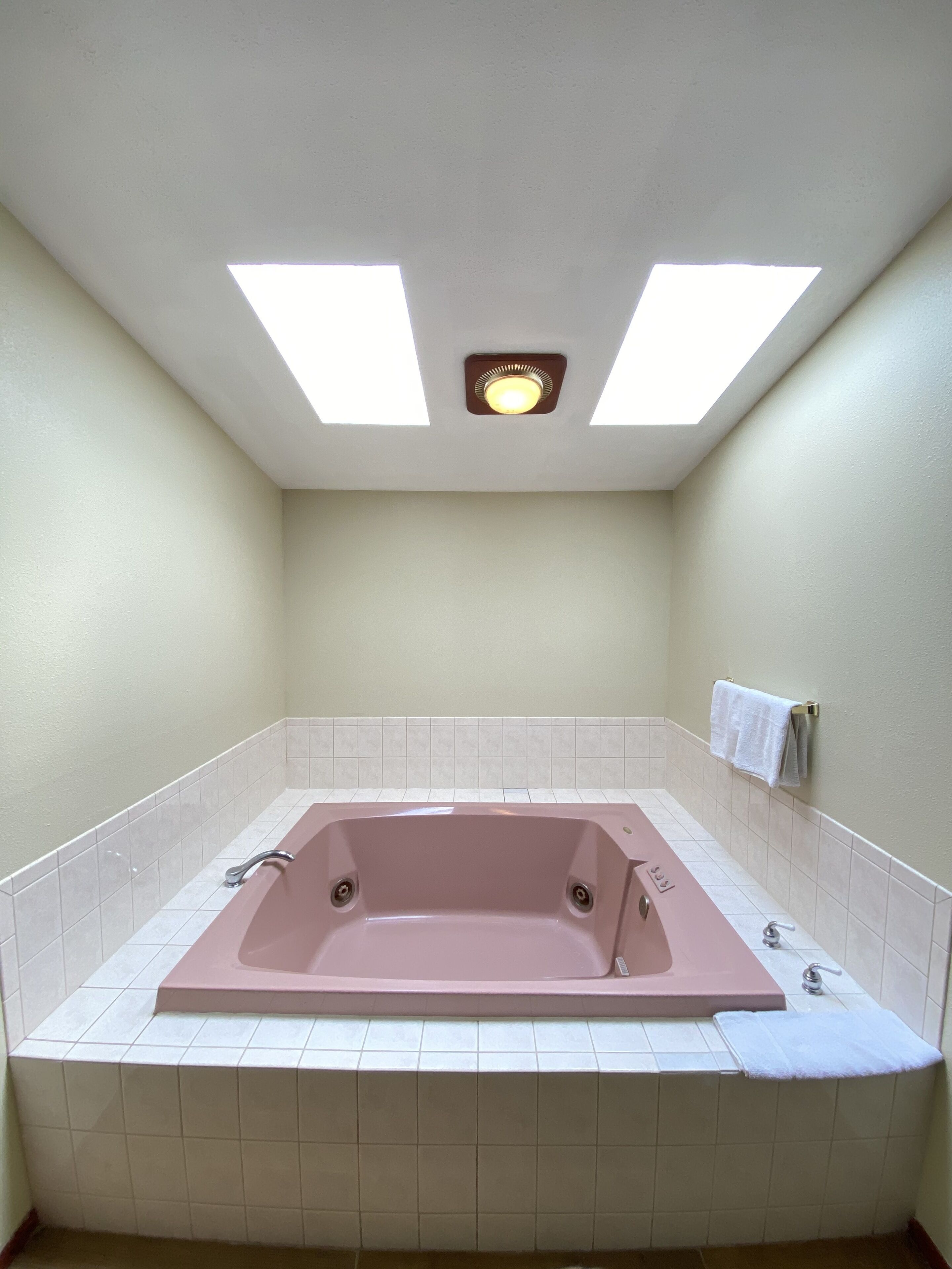 A bathroom with a large bathtub, white tiled walls, and a skylight above.