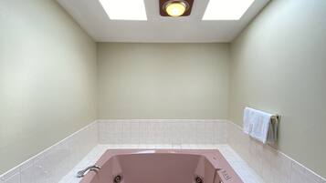 A bathroom with a large bathtub, white tiled walls, and a skylight above.