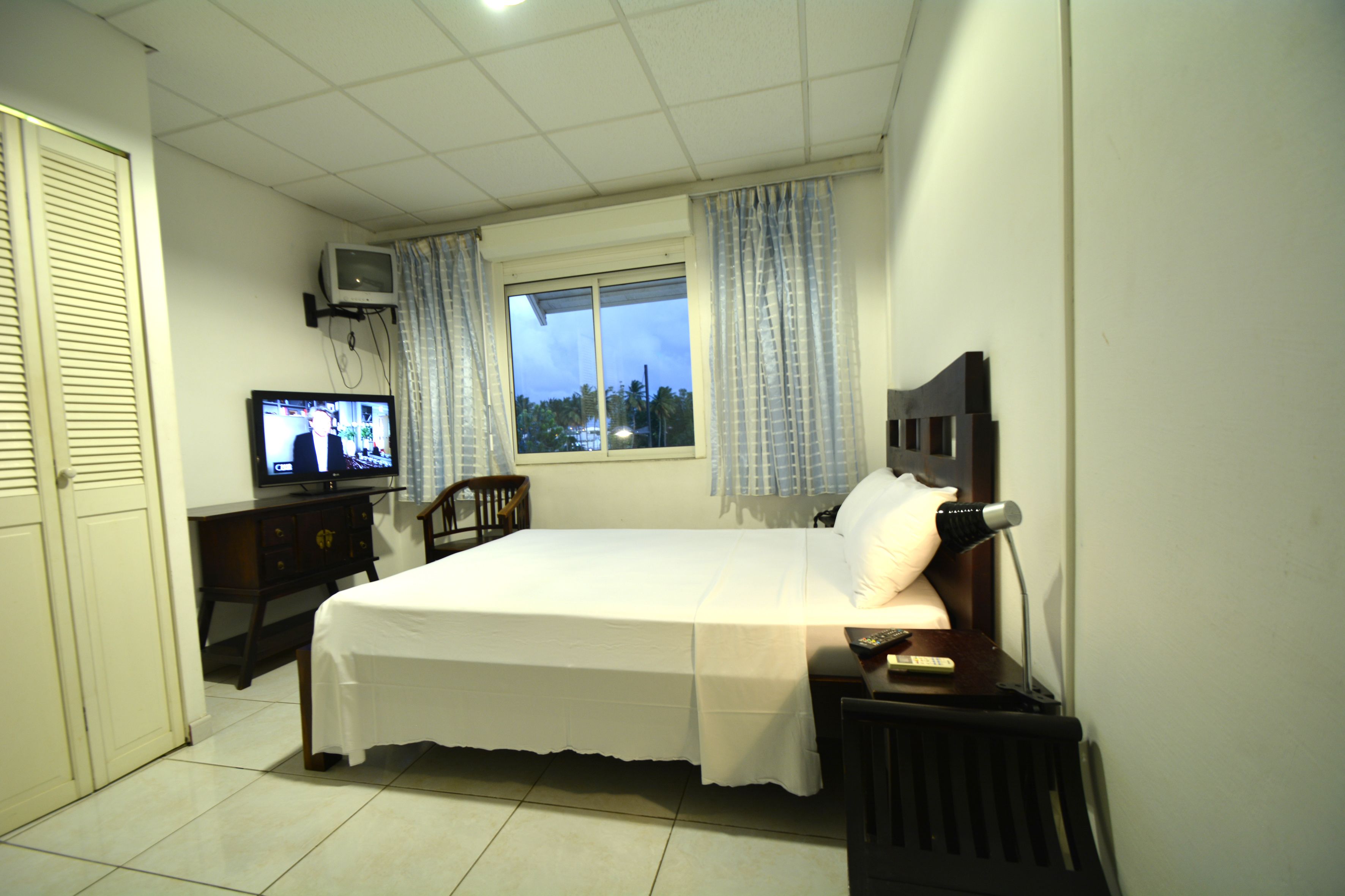 Ein Schlafzimmer mit Bett, Fernseher, Schreibtisch und einem Fenster mit Vorhängen.