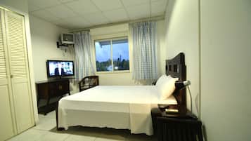Une chambre à coucher avec un lit, une télévision, un bureau et une fenêtre avec des rideaux.