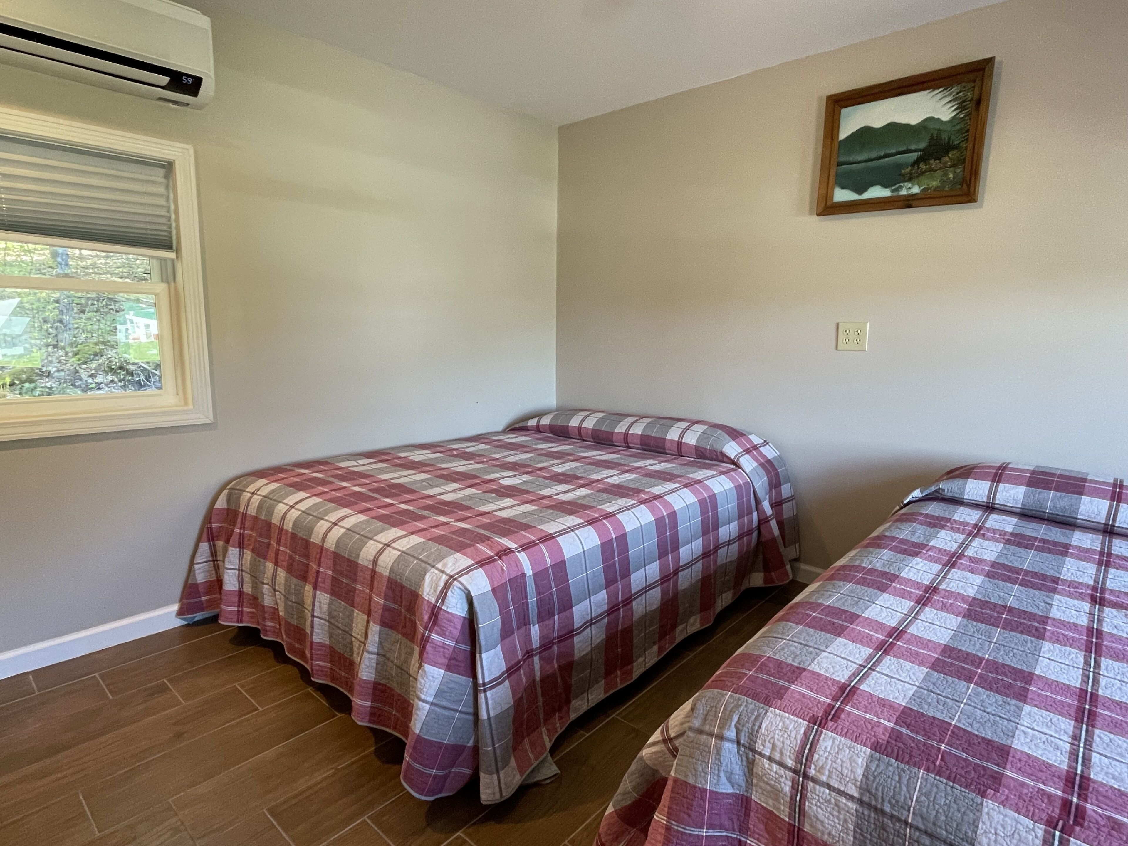 A room with two beds, a window with blinds, a painting on the wall, and a thermostat above the window.