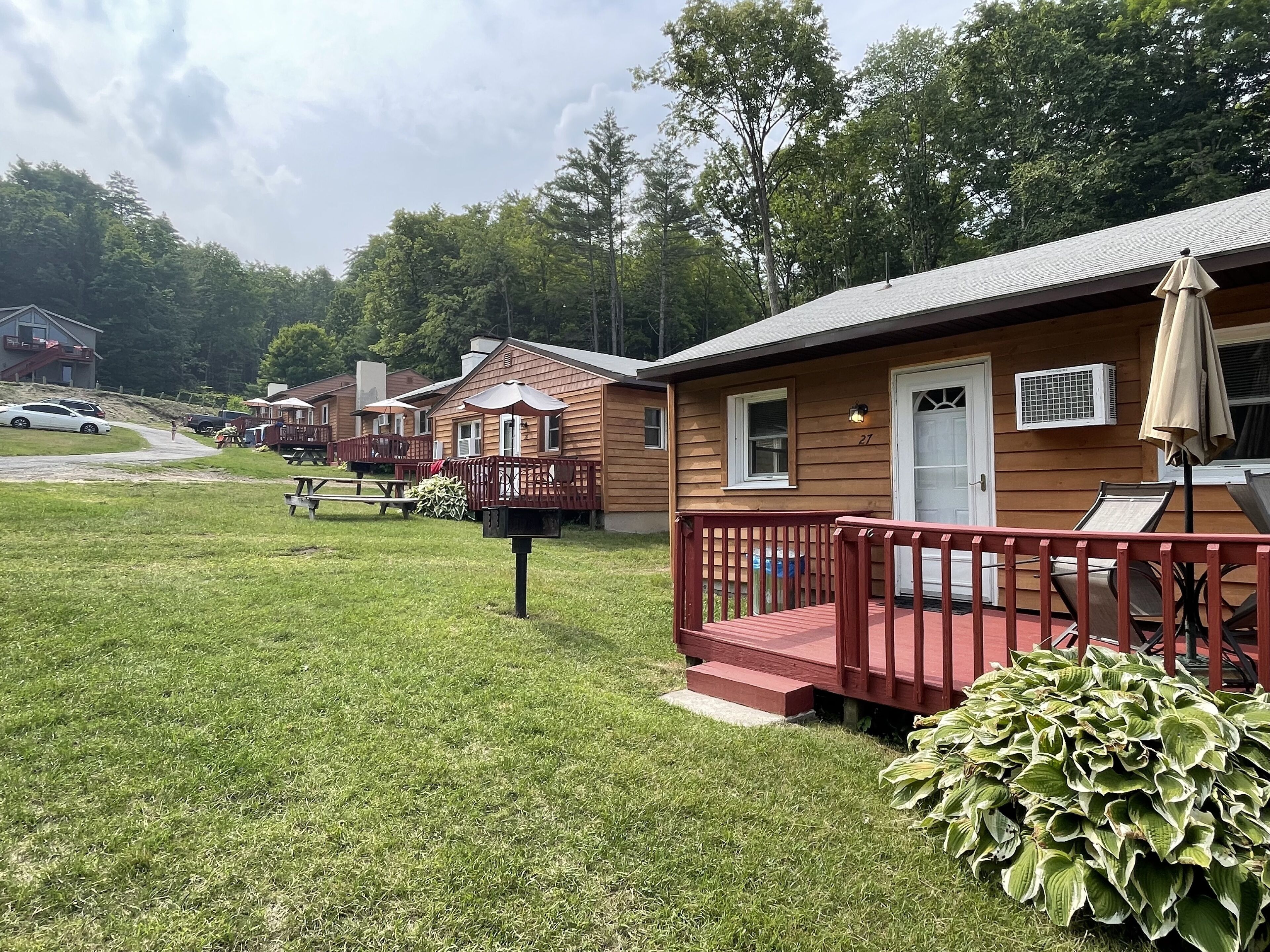 A row of wooden cabins with a grassy lawn, picnic tables, and a mailbox.
