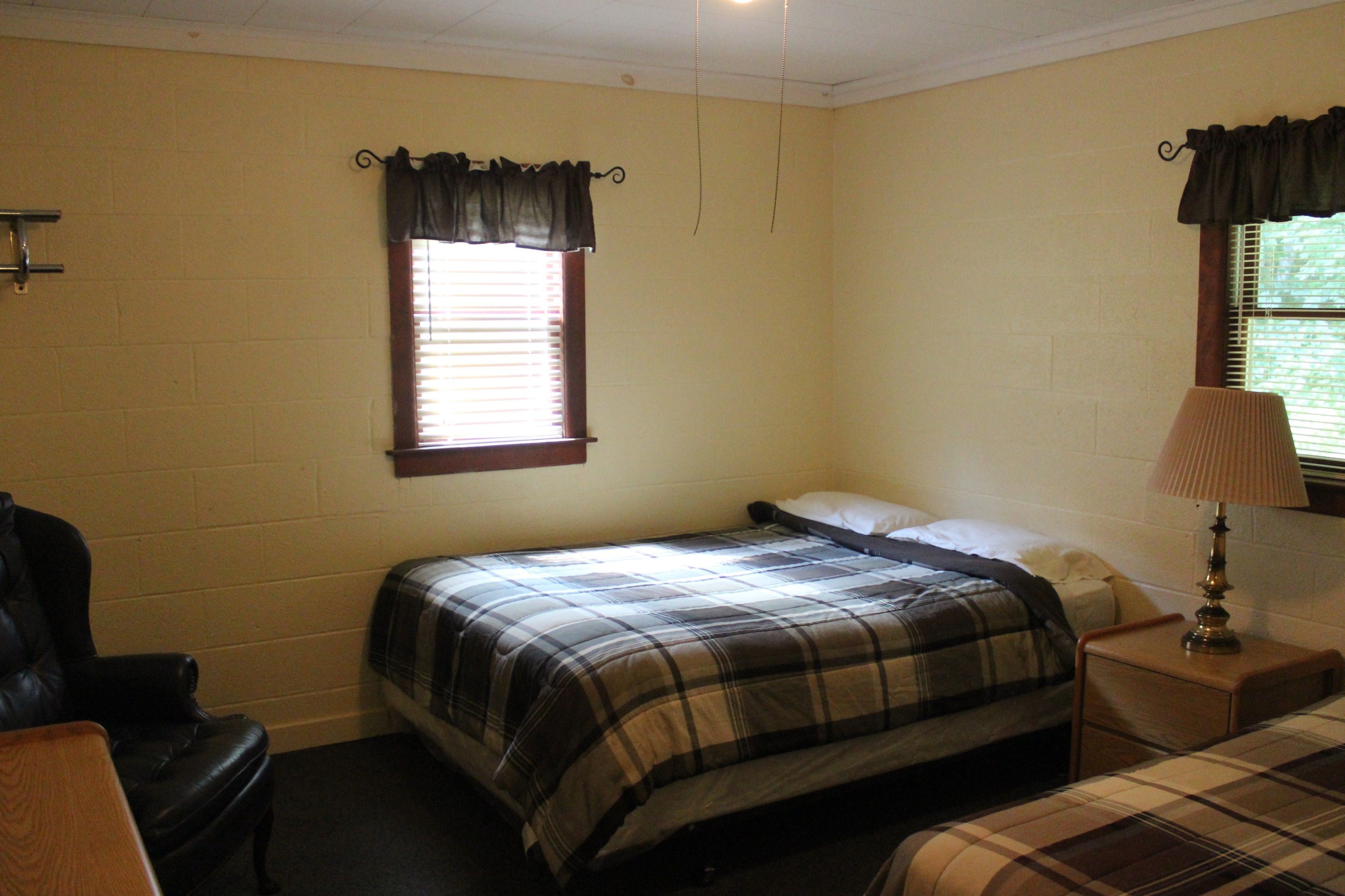 A bedroom with a single bed, a nightstand, a chair, and a window with curtains.