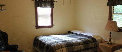 A bedroom with a single bed, a nightstand, a chair, and a window with curtains.