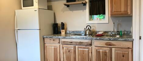 A kitchen with a white refrigerator, wooden cabinets, a microwave, a kettle, and a coffee maker.