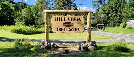 Placa de madeira para Hill View Cottages com ilustração de montanha.
