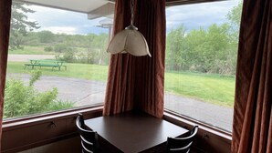 A corner room with a table and chairs, large windows with curtains, and a hanging light fixture. - Crossroads Motel (Elkhorn)
