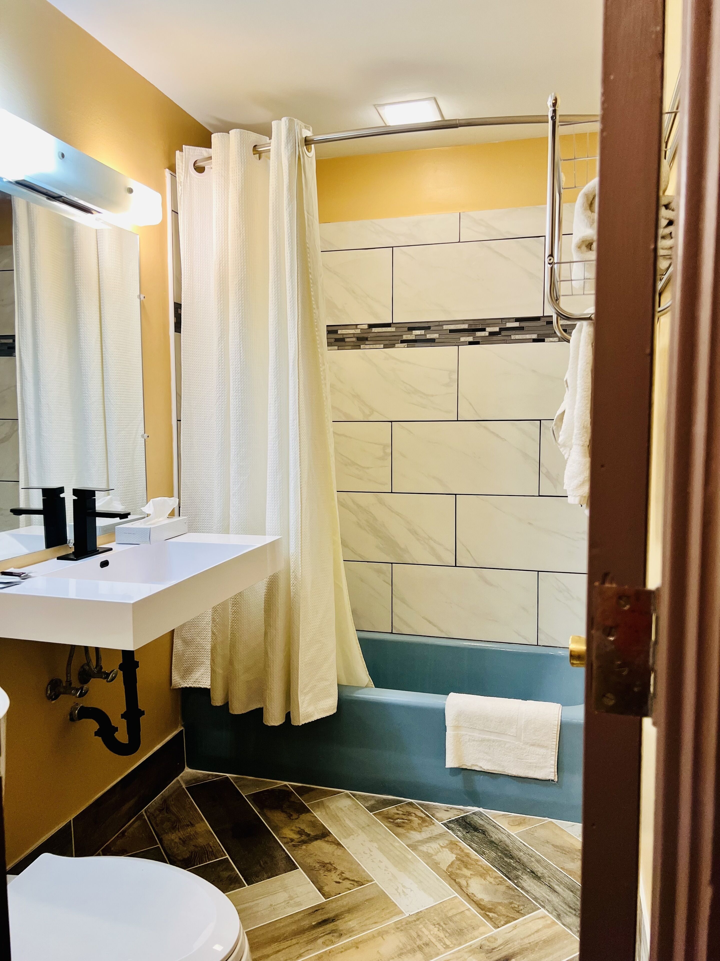 Et badeværelse med hvid vask, toilet, bruser med badeforhæng og badekar.
