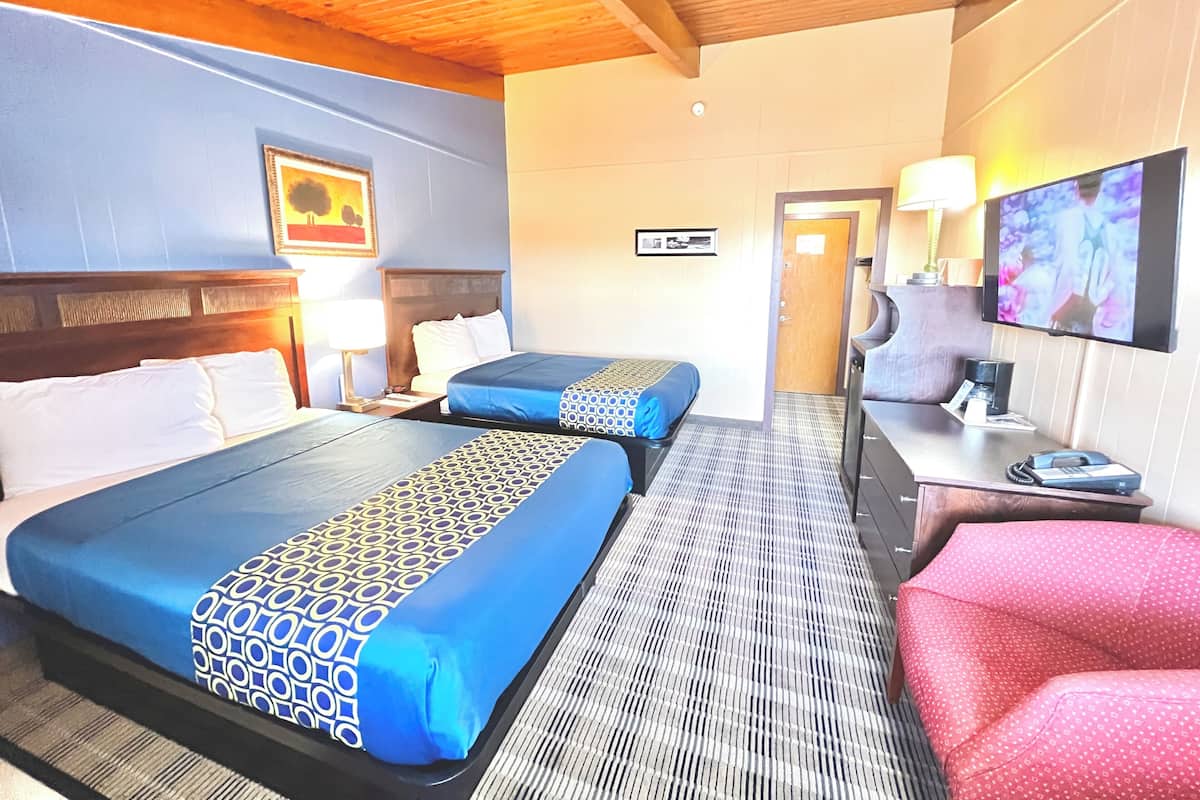 Quarto de hotel com duas camas, uma televisão, uma escrivaninha com candeeiro e uma cadeira vermelha.