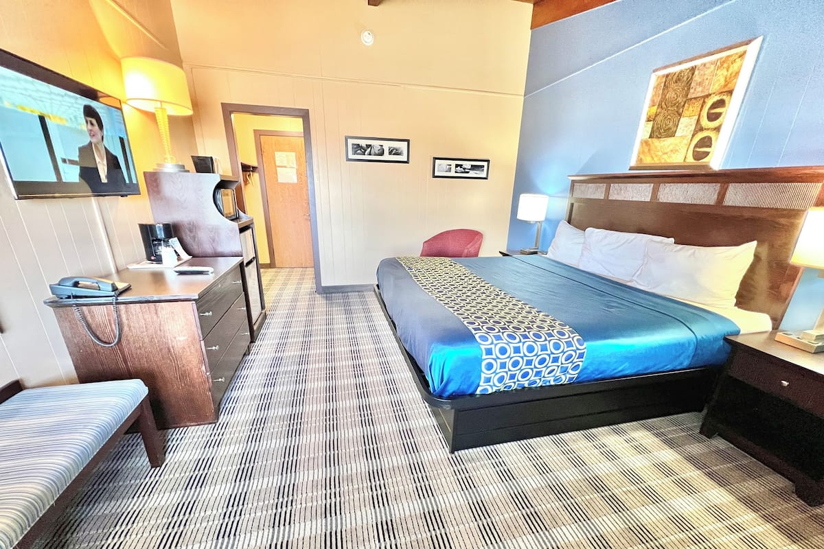 Quarto de hotel com cama, escrivaninha, cadeira, TV e parede com quadros emoldurados.