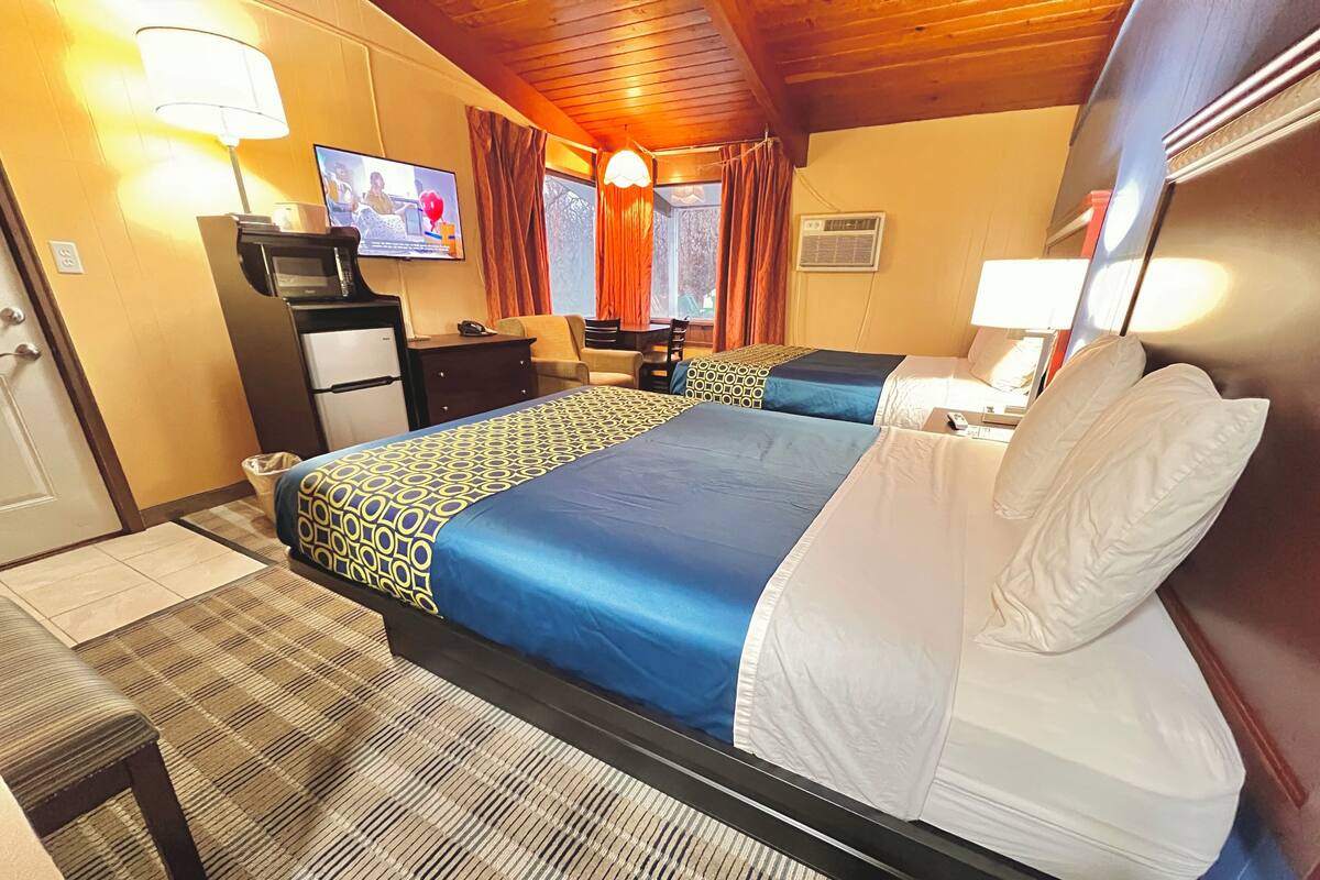 Quarto de hotel com uma cama grande, escrivaninha, televisão e janela com cortinas.