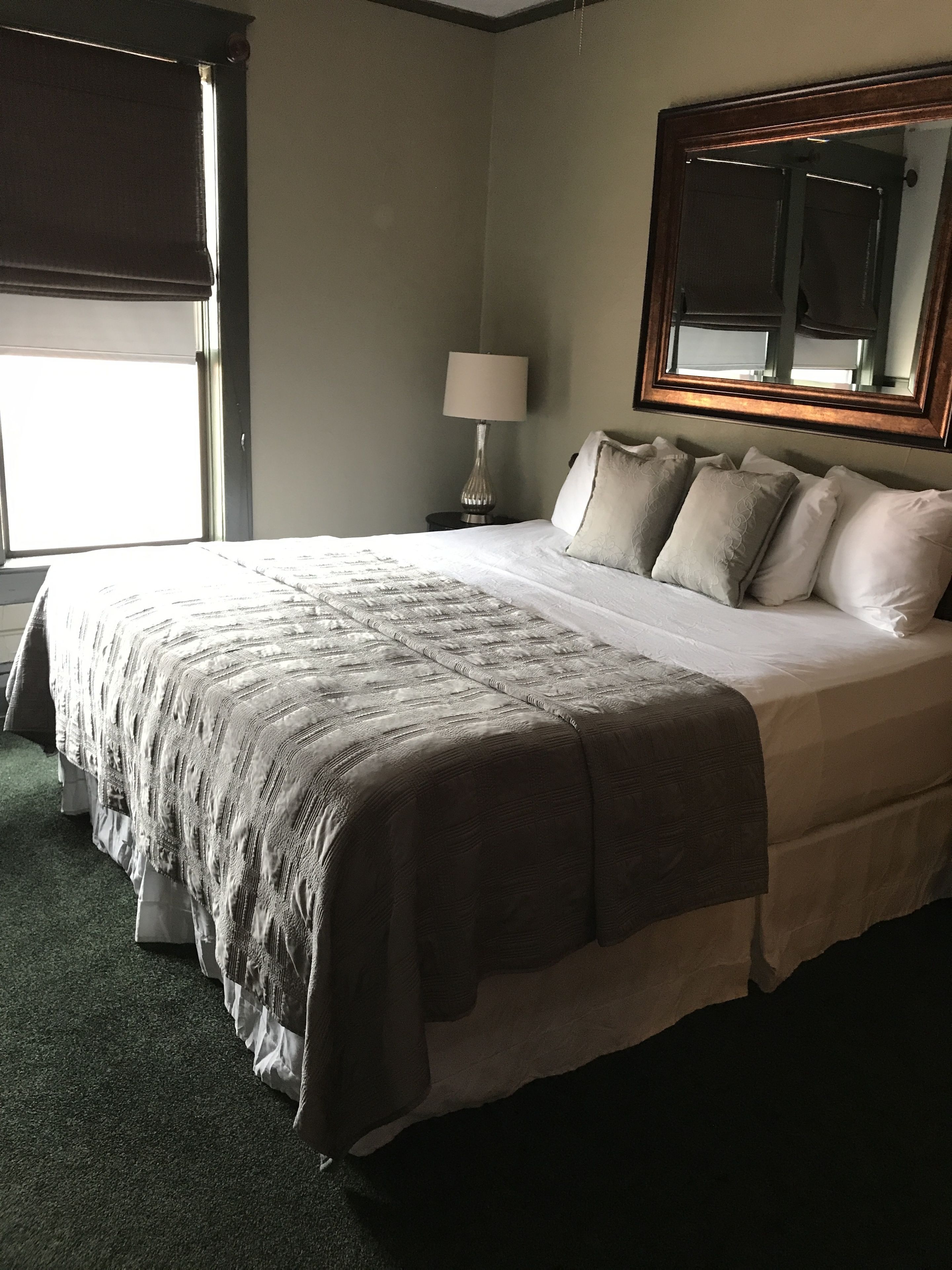 Una cama bien hecha con una colcha estampada, una lámpara de noche y un espejo grande sobre la cama.