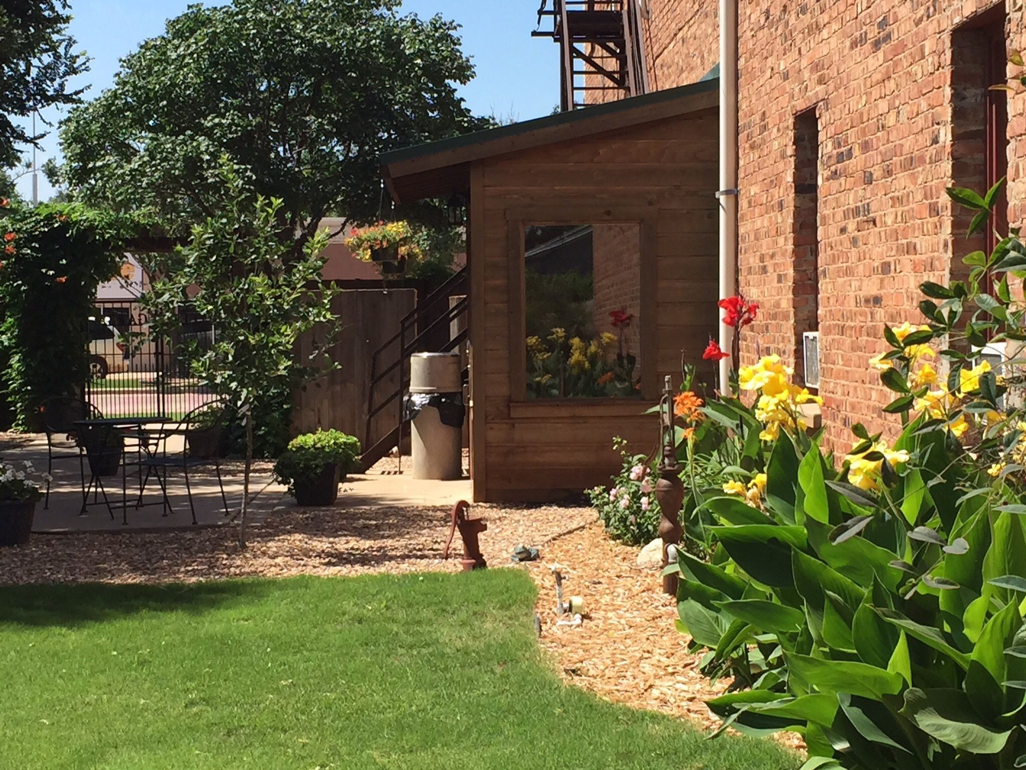 A brick building with a wooden deck, outdoor seating, and a garden with various plants and flowers.