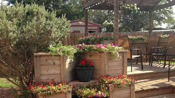 A wooden deck with planters containing flowers, a pergola, and outdoor furniture.