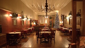 Un comedor con cálida iluminación, mesas y sillas de madera, un candelabro y un árbol de Navidad.