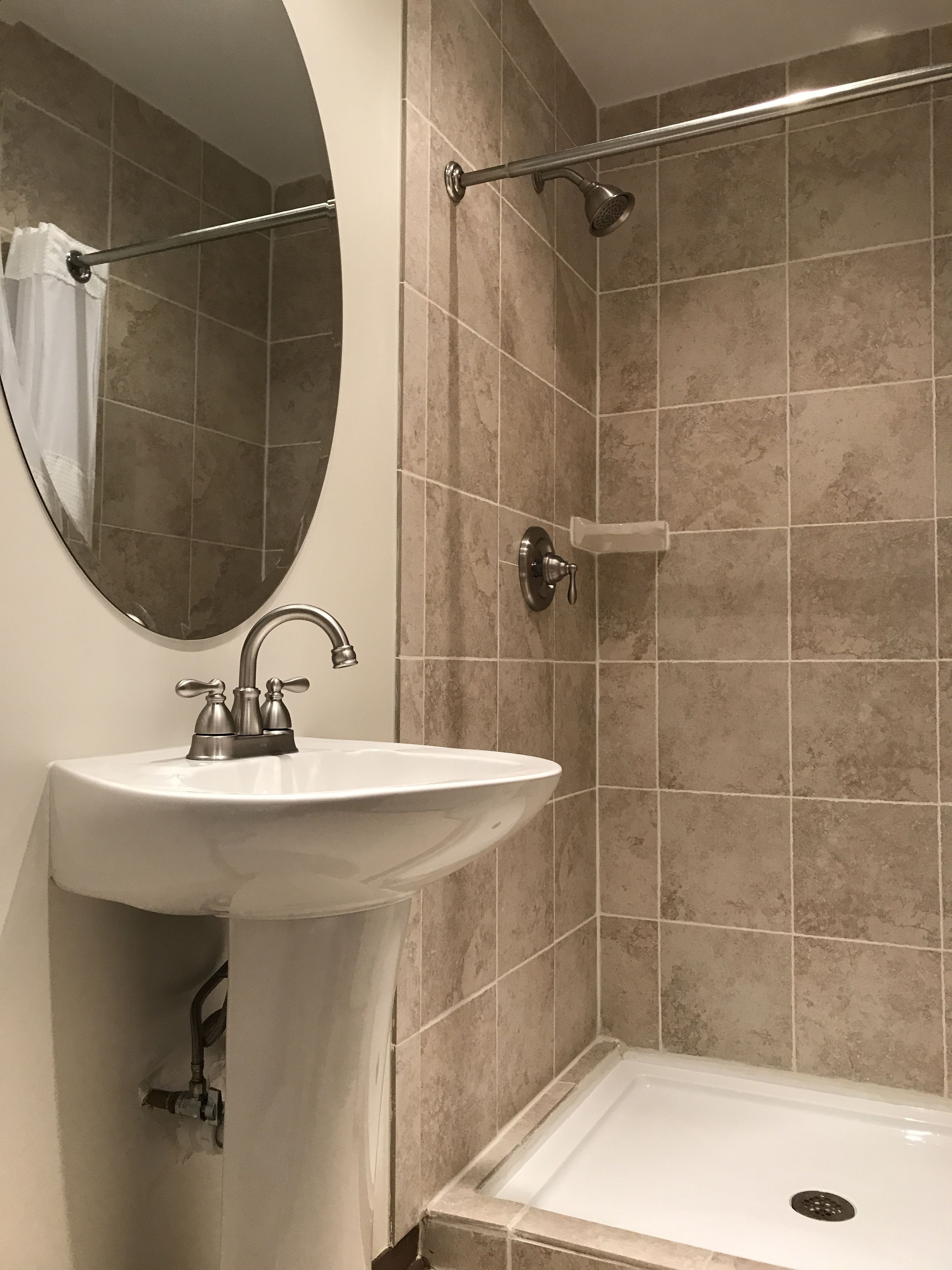 A bathroom with a white sink, a mirror, a shower with a handheld showerhead, and beige tiled walls.