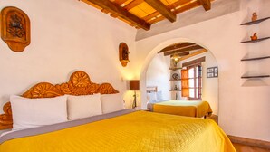 A room with a large bed, wooden headboard, and a yellow bedspread. There is a wooden shelf with decorative items on the wall.
