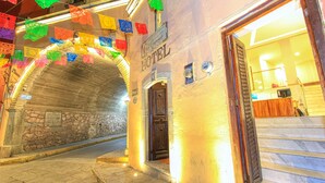 A hotel entrance with a stone archway, a sign indicating the hotel's name, and a staircase leading inside.