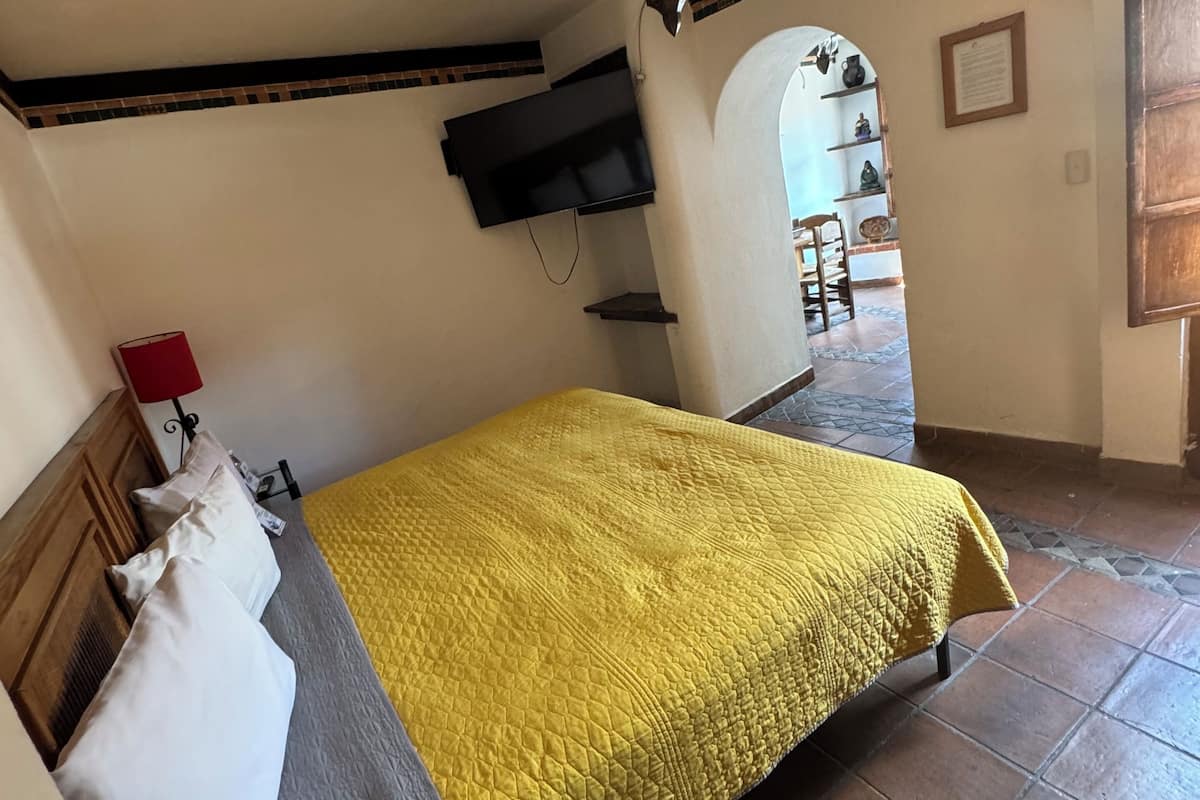 A bedroom with a bed, a TV mounted on the wall, a red lamp, and a tiled floor.