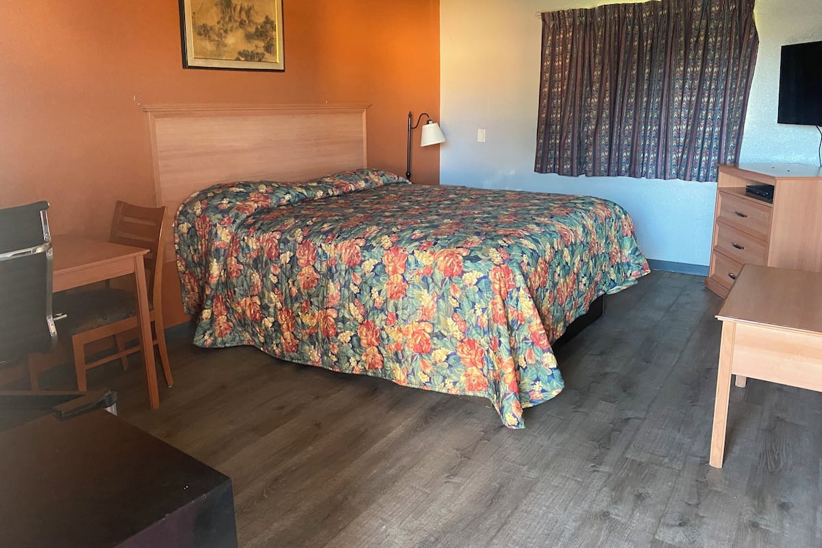 A room with a bed, a desk, a chair, a lamp, and a television.