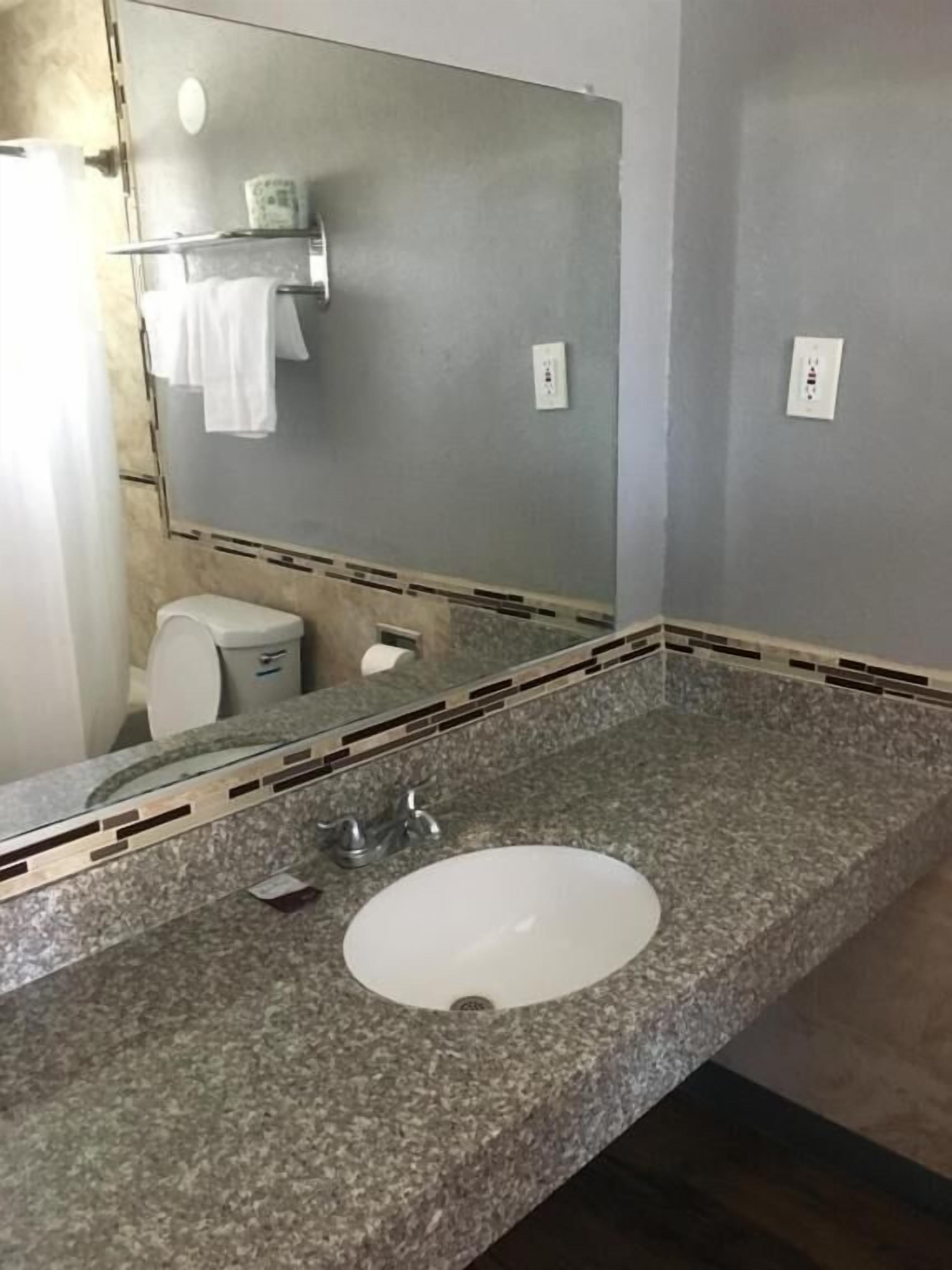 A bathroom with a granite countertop, a white sink, and a large mirror.