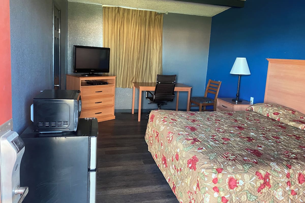 A hotel room with a bed, a desk with a chair, a television, a dresser, and a lamp.