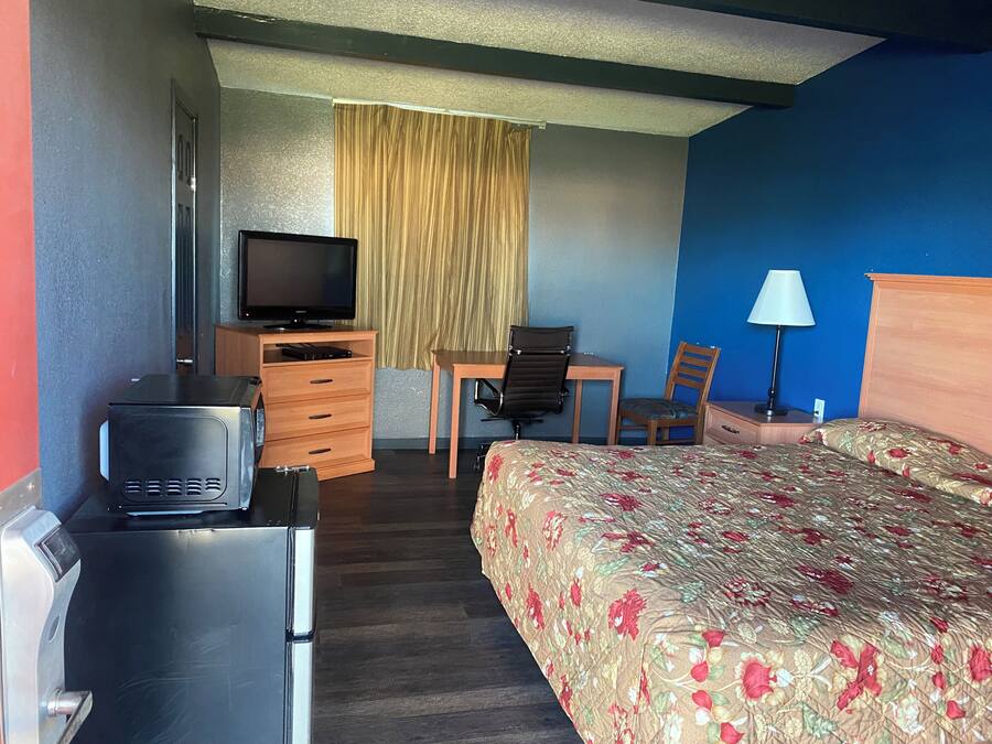 Una habitación de hotel con una cama, un escritorio con silla, televisión, cómoda y una lámpara.