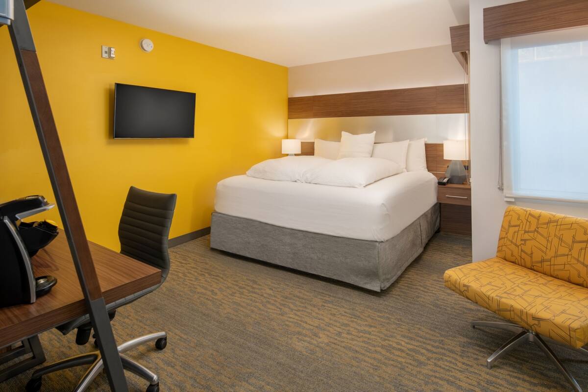 A hotel room with a bed, a desk, a chair, a TV, and a window.