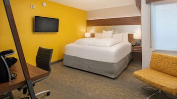 A hotel room with a bed, a desk, a chair, a TV, and a window.