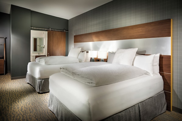 A hotel room with two beds, a large mirror, a wooden headboard, and a carpeted floor.