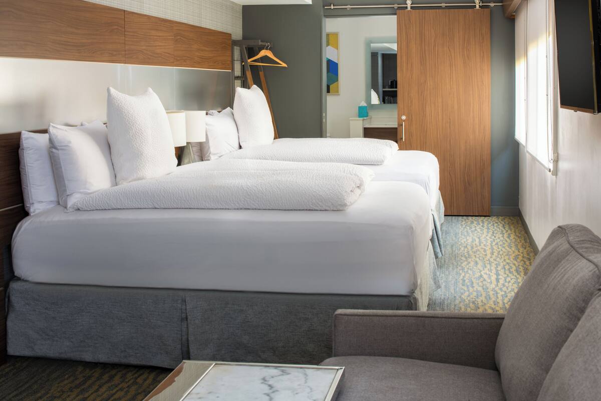 A hotel room with two beds, a sofa, a bedside table, a wardrobe, and a mirror.