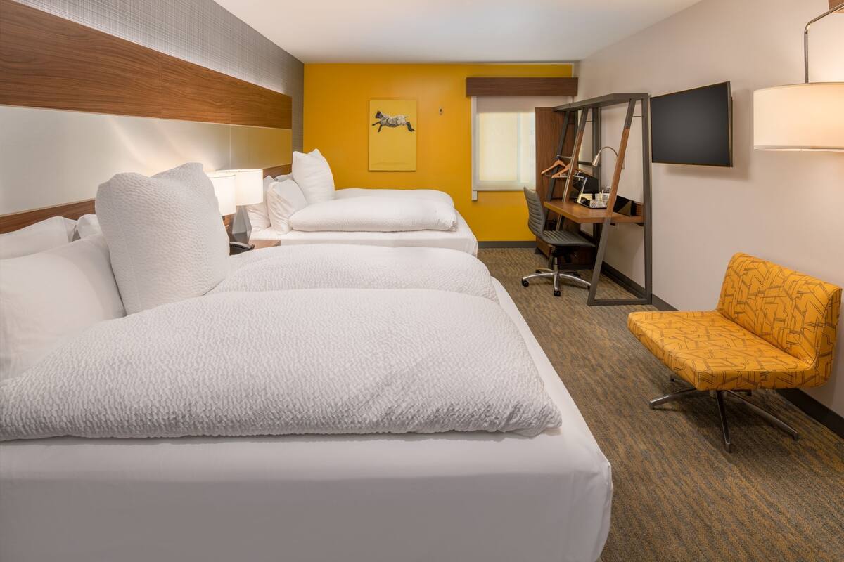 A hotel room with two beds, a desk, a chair, a TV, and a window.