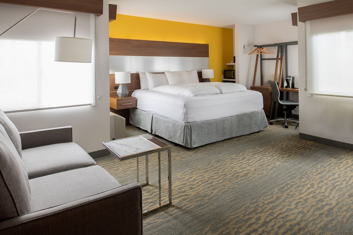 A hotel room with a bed, a desk, a chair, a lamp, and a wardrobe.