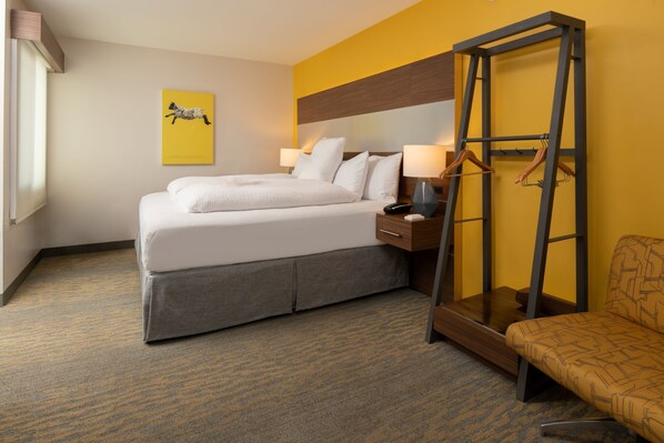 Une chambre d’hôtel comprenant un lit, une table de chevet, une lampe et un miroir avec un porte-manteau.