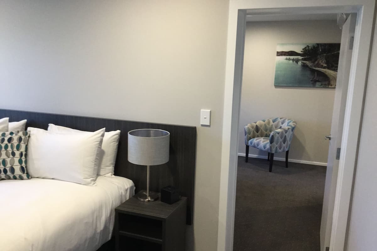 A hotel room with a bed, a nightstand, a lamp, and a chair.