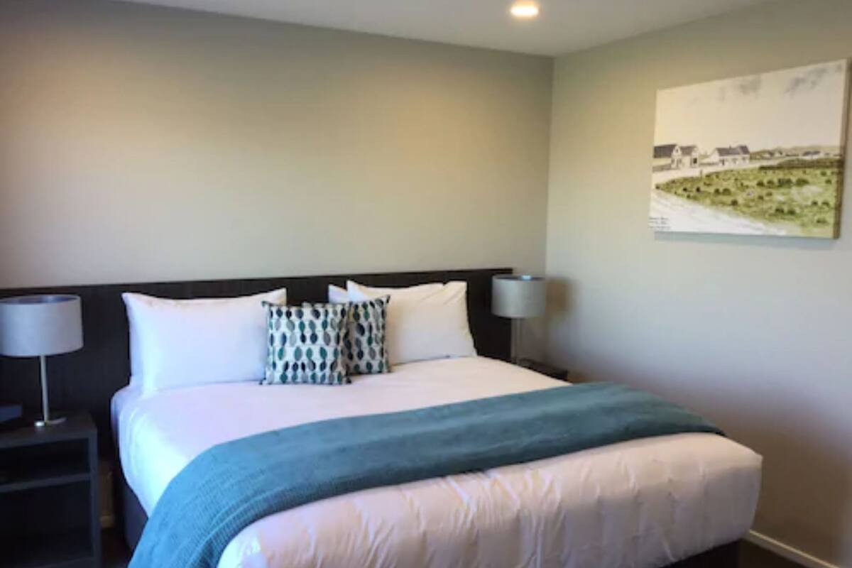 A hotel room with a bed, two bedside lamps, a painting on the wall, and a nightstand.