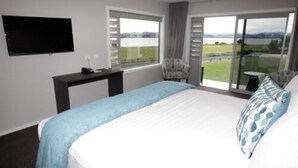A bedroom with a large bed, a desk, a chair, and a TV on the wall. - East Pier Hotel (Napier)