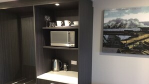 A kitchen with dark cabinetry, a microwave, a kettle, and a coffee maker. There's a framed picture on the wall. - East Pier Hotel (Napier)