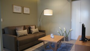 Una sala de estar con un sofá marrón, una mesa de centro, una lámpara de pie, un jarrón con flores y un televisor sobre un mueble.