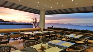 An outdoor dining area with tables and chairs, overlooking a scenic view of the sea and mountains during sunset. - El Nido Bayview Resort (El Nido)