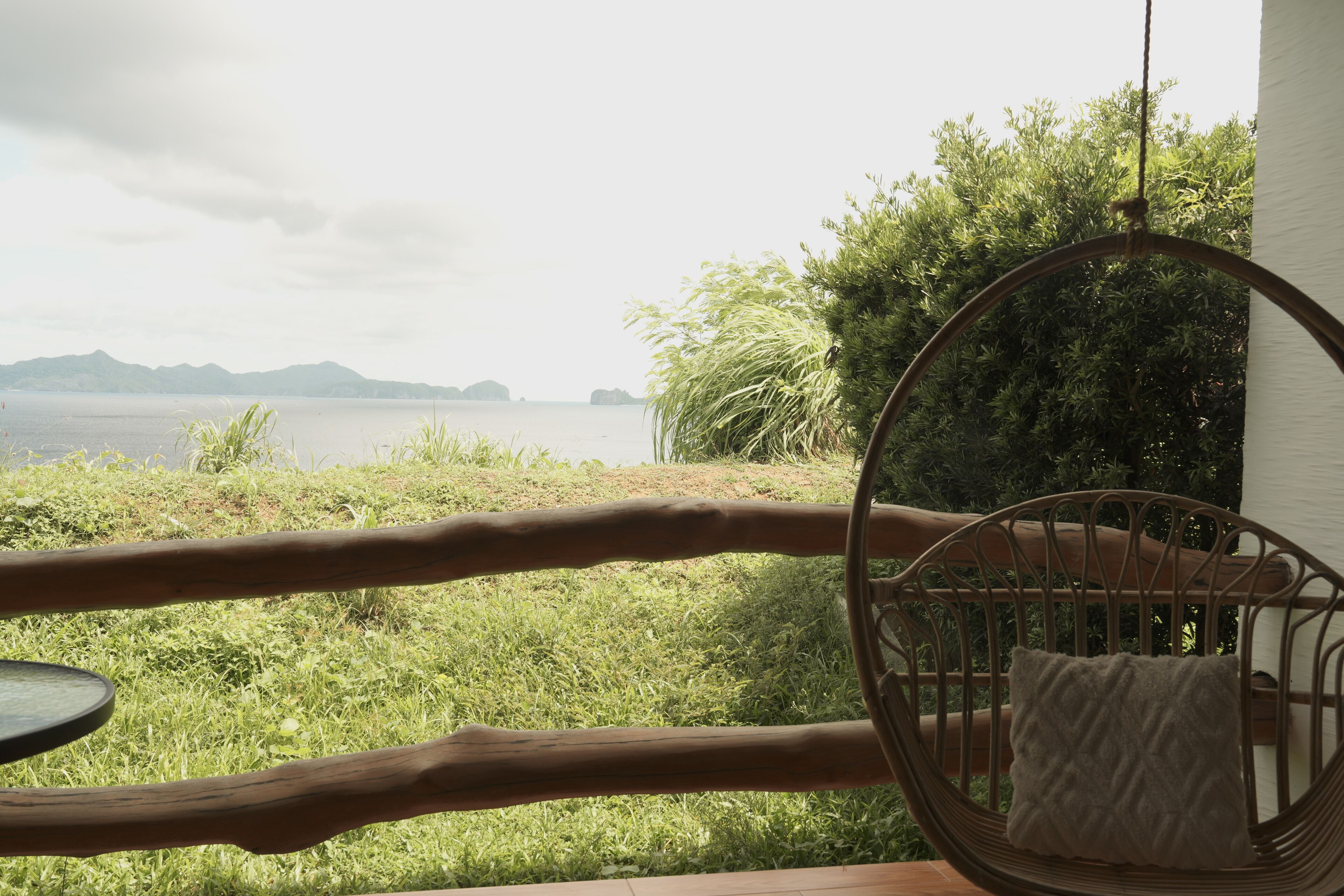 A wicker chair with a cushion, overlooking a grassy area with a view of the sea and distant mountains.