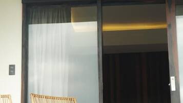 Quarto com uma cama, porta de vidro deslizante e duas cadeiras de vime.