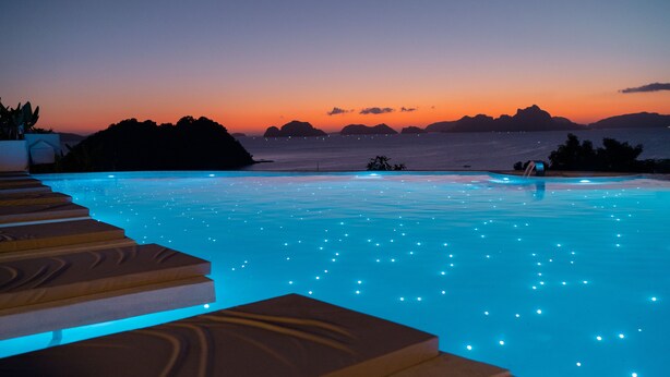 A pool with illuminated steps and a view of the ocean at dusk. - El Nido Bayview Resort (El Nido)