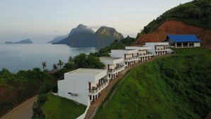 A coastal hotel with multiple white buildings, a blue-roofed structure, and a view of the sea and mountains. - El Nido Bayview Resort (El Nido)