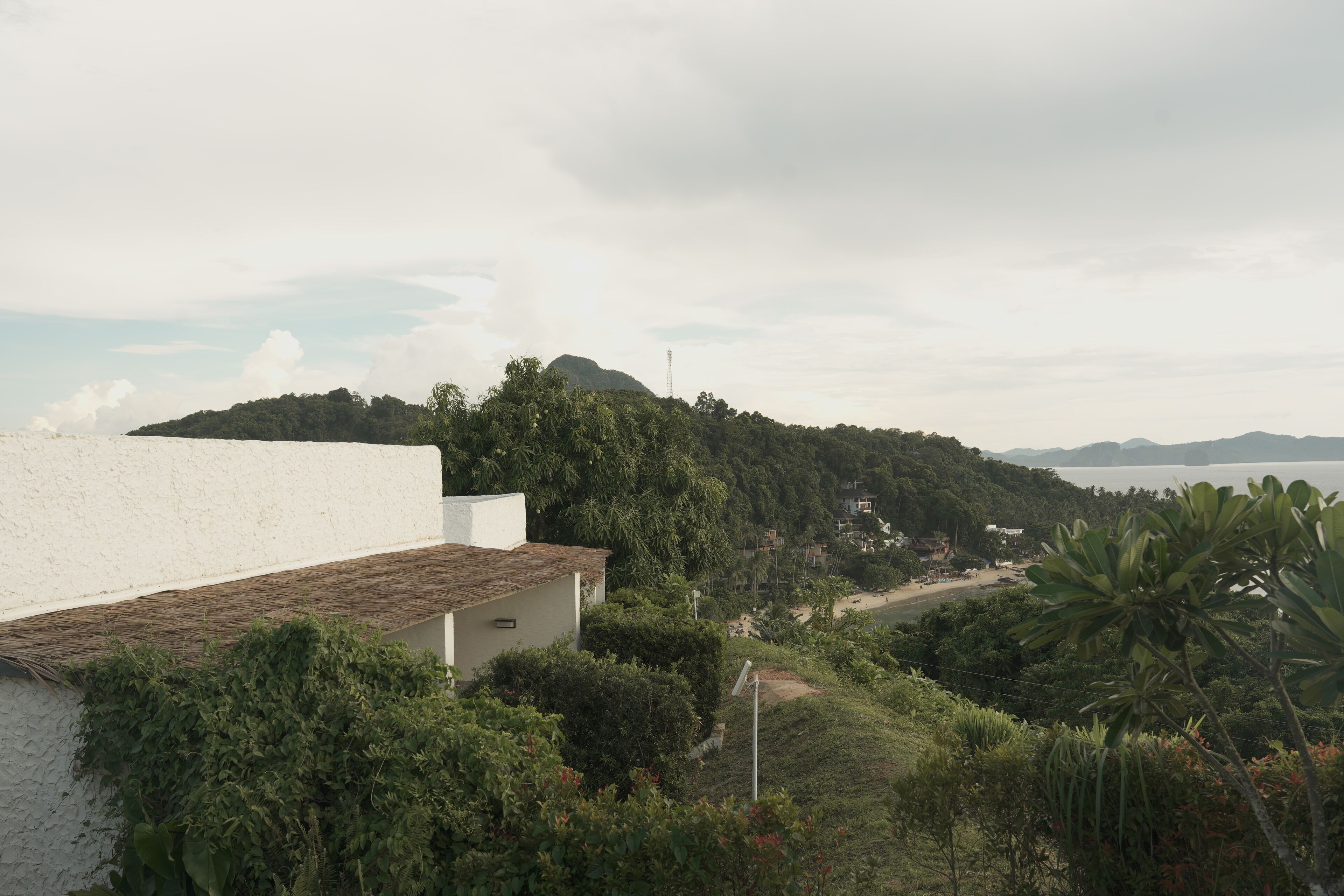 A coastal landscape with a white building, lush greenery, and a distant view of the sea.